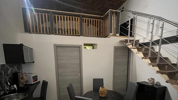 A compact living space with a dining area, a kitchen, and a staircase leading to an upper level. - Becial house (Napoli)