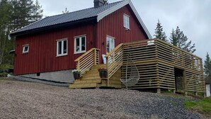 Una casa de madera roja con techo gris, una escalera de madera y un camino de entrada de grava.