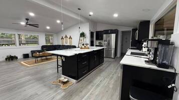 A modern kitchen with a central island, black cabinetry, stainless steel appliances, and a large window providing natural light.