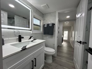 Un baño moderno con tocador blanco, un espejo grande y un salpicadero de mármol.