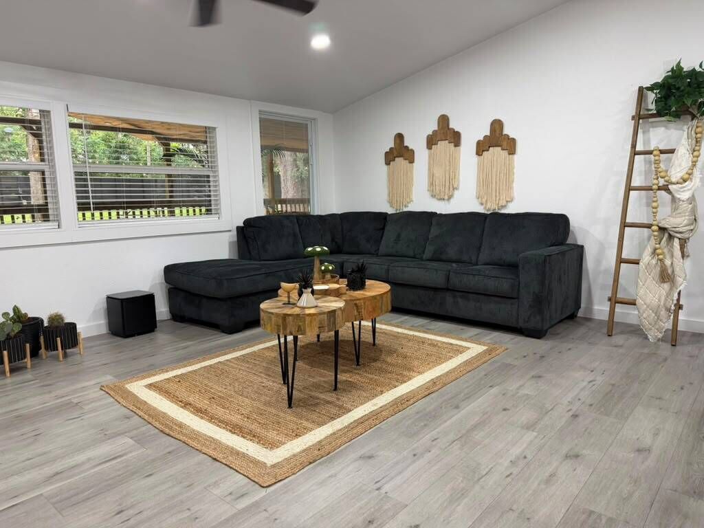A modern living room with a dark grey sectional sofa, a round wooden coffee table, and a woven rug.