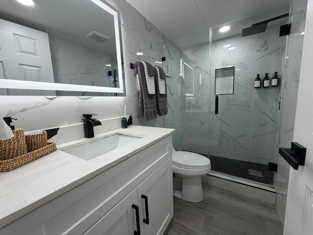 A modern bathroom with a white marble vanity, a glass shower enclosure, and a white toilet.