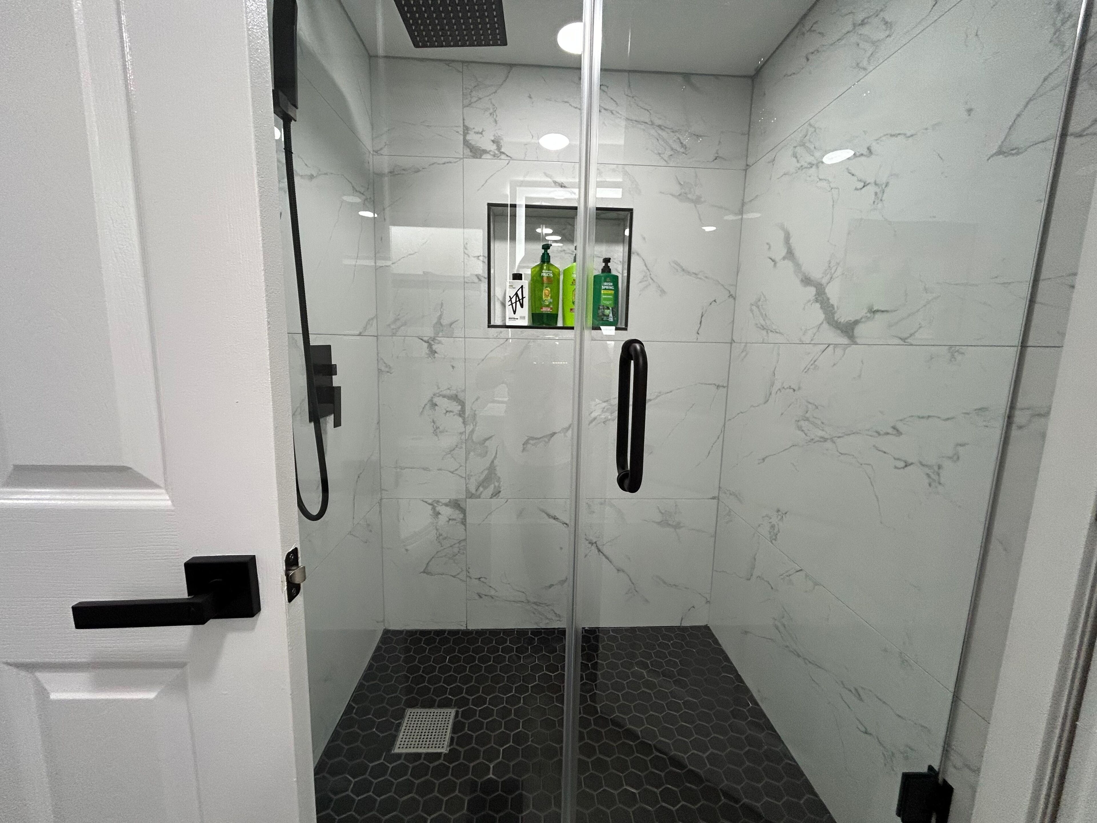 Ein modernes Duschbad mit Glastür, Marmorwänden und einem sechseckigen Fliesenspiegel.