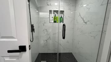 Ein modernes Duschbad mit Glastür, Marmorwänden und einem sechseckigen Fliesenspiegel.