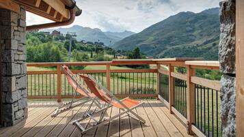 A wooden deck with a view of mountains, a stone wall, and a lounge chair.