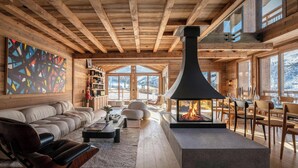 Interior acogedor de una cabaña de troncos con chimenea, vigas de madera y ventanas amplias con vistas a las montañas.