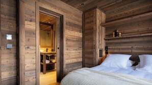 Un dormitorio con paneles de madera, una cama, una mesita de noche y una puerta de madera que da a un baño.