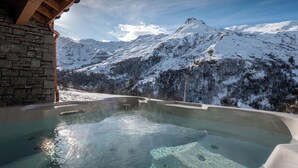 Un jacuzzi con vista a la montaña, paredes de piedra y vigas de madera.