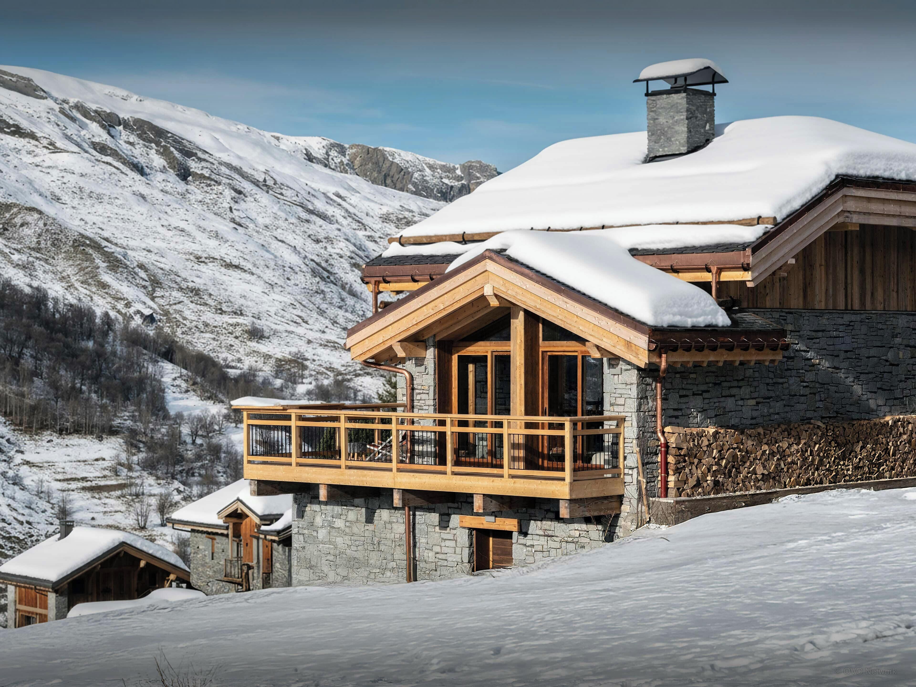 Un chalet avec une façade en pierre, un balcon en bois et une cheminée.