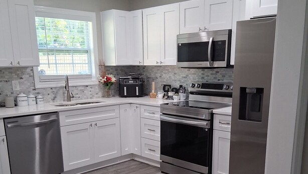 A modern kitchen with white cabinets, stainless steel appliances, and a wooden floor. - ABM Southern Vacation Rental 
3-bedroom house in marvelous Savannah with WiFi (Savannah)