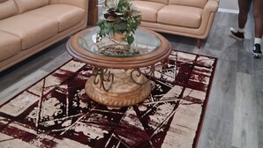 A living room with two beige sofas, a glass coffee table with a plant, a patterned rug, and a ceiling fan. - ABM Southern Vacation Rental 
3-bedroom house in marvelous Savannah with WiFi (Savannah)