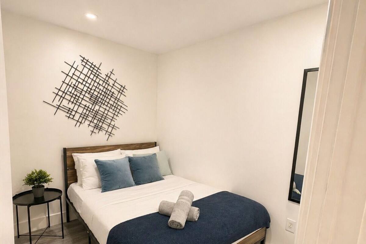 Une chambre à coucher moderne avec un cadre de lit en bois, une couvre-lit bleu foncé et une décoration murale aux motifs géométriques.
