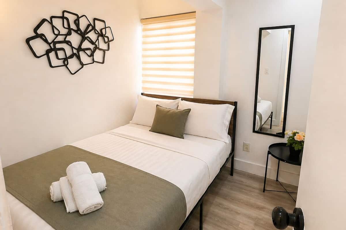 Une chambre moderne avec un lit, une œuvre d’art abstraite accrochée au mur, un miroir de chevet et une petite table sur laquelle est posée une plante.