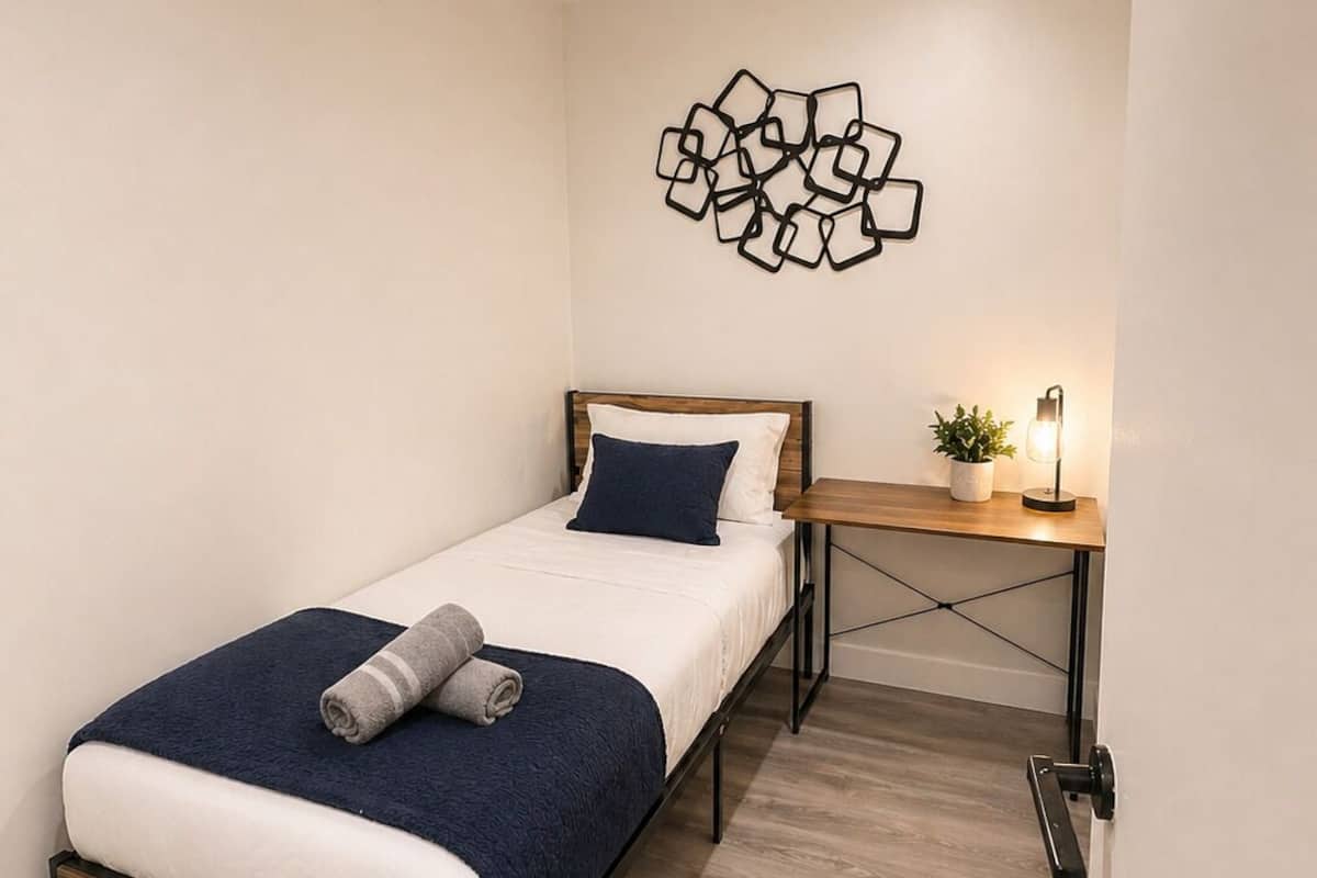 Une chambre avec un lit, un bureau, une œuvre d’art murale et une petite plante.
