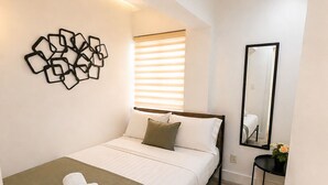 Een moderne slaapkamer met een bed, een wanddecoratie in abstractie, een spiegel naast het bed en een klein tafeltje met een plantje.