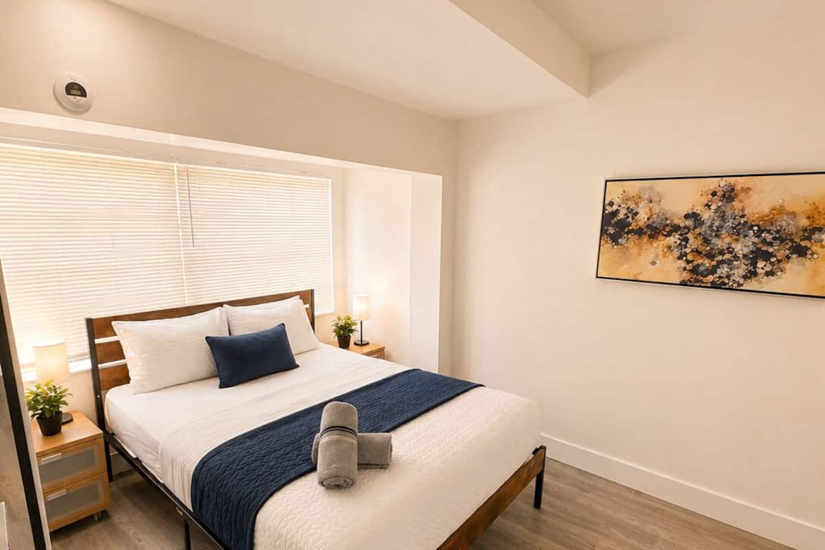 Une chambre à coucher moderne, comprenant un lit, des tables de chevet, une commode, une œuvre d’art accrochée au mur et un luminaire au plafond.