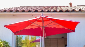 A patio with a red umbrella, two red chairs, and a glass door leading to a kitchen. - Studio for 3 people – Shared pool (Les Sables-d´Olonne)