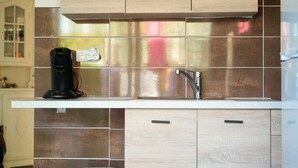 A kitchen with a stainless steel sink, a coffee maker, and wooden cabinets. - Studio for 3 people – Shared pool (Les Sables-d´Olonne)