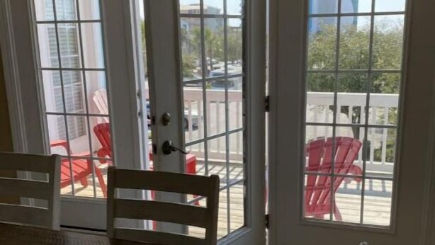 Et spiseområde med et bord og stole, samt en skydedør der fører ud til en udendørs terrasse med røde stole.