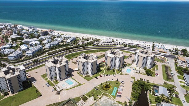An aerial view of a coastal residential area with high-rise buildings, a beach, and a swimming pool.
