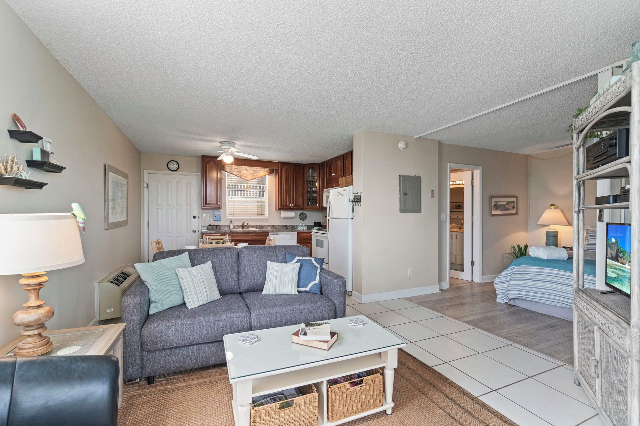 A compact living space with a kitchenette, a gray sofa, a white coffee table, and a television.