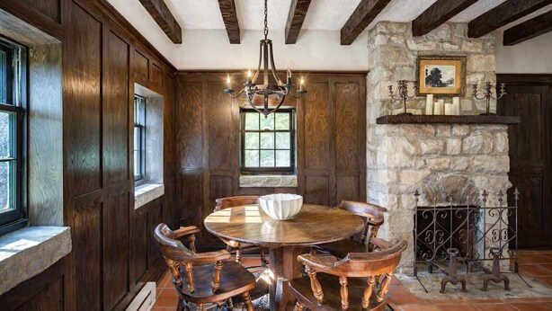 A dining room with a round wooden table, six wooden chairs, a chandelier, stone fireplace, and wooden paneling. - Storybook Cottage with Fireplace (Banner Elk)