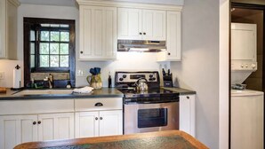 A kitchen with white cabinets, a stove, and a sink. - Storybook Cottage with Fireplace (Banner Elk)