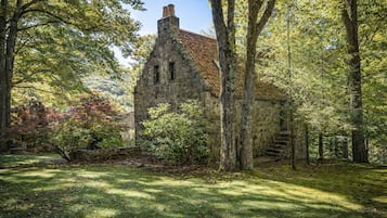 A stone building with a steep roof, surrounded by trees and a grassy area.