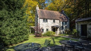A stone building with a garden patio featuring metal tables and chairs. - Storybook Cottage with Fireplace (Banner Elk)