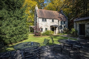 Ein Steinhaus mit Garten und einer Terrasse, die Metalltische und -stühle bietet.