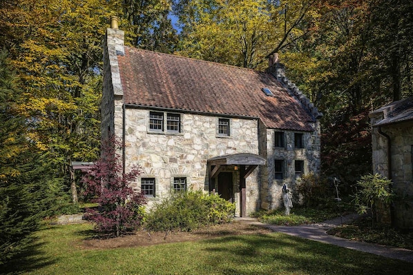 Ein Steinhaus mit geneigtem Dach, einer Veranda und einem gepflegten Garten.