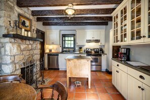 A kitchen with white cabinets, a wooden island, a stone wall, and a tiled floor.