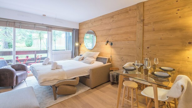 A modern bedroom with a large bed, a glass dining table, and a wooden wall.