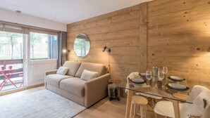 A modern living room with a wooden wall, a round mirror, a sofa, a glass dining table set with plates and glasses, and a small stool.
