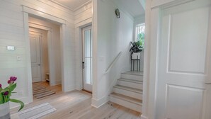 Ein Flur mit weißen Wänden und Holzböden, der zu einer Treppe mit einem kleinen Tisch und Pflanzen führt.