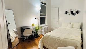A bedroom with a bed, a desk, a chair, a mirror, and a radiator. - Cozy house (Jersey City)