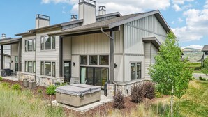 Une maison moderne à deux étages, dotée d’un patio couvert, de fondations en pierre et offrant une vue sur le paysage environnant.