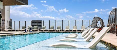 A swimming pool with lounge chairs and a view of a cityscape.
