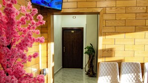 A reception area with a TV mounted on the wall, a potted pink tree, and a seating area with chairs. - Mountain Echo Inn (At-Taybeh)