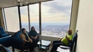 A spacious living room with large windows, a chandelier, and a view of a cityscape. - Mountain Echo Inn (At-Taybeh)