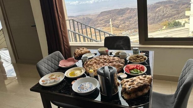 A dining table set with various dishes, a kettle, and a view of mountains through a window. - Mountain Echo Inn (At-Taybeh)