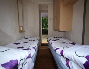 Een kamer met twee bedden, een houten kledingkast, een spiegel en een deur naar een buitenruimte.