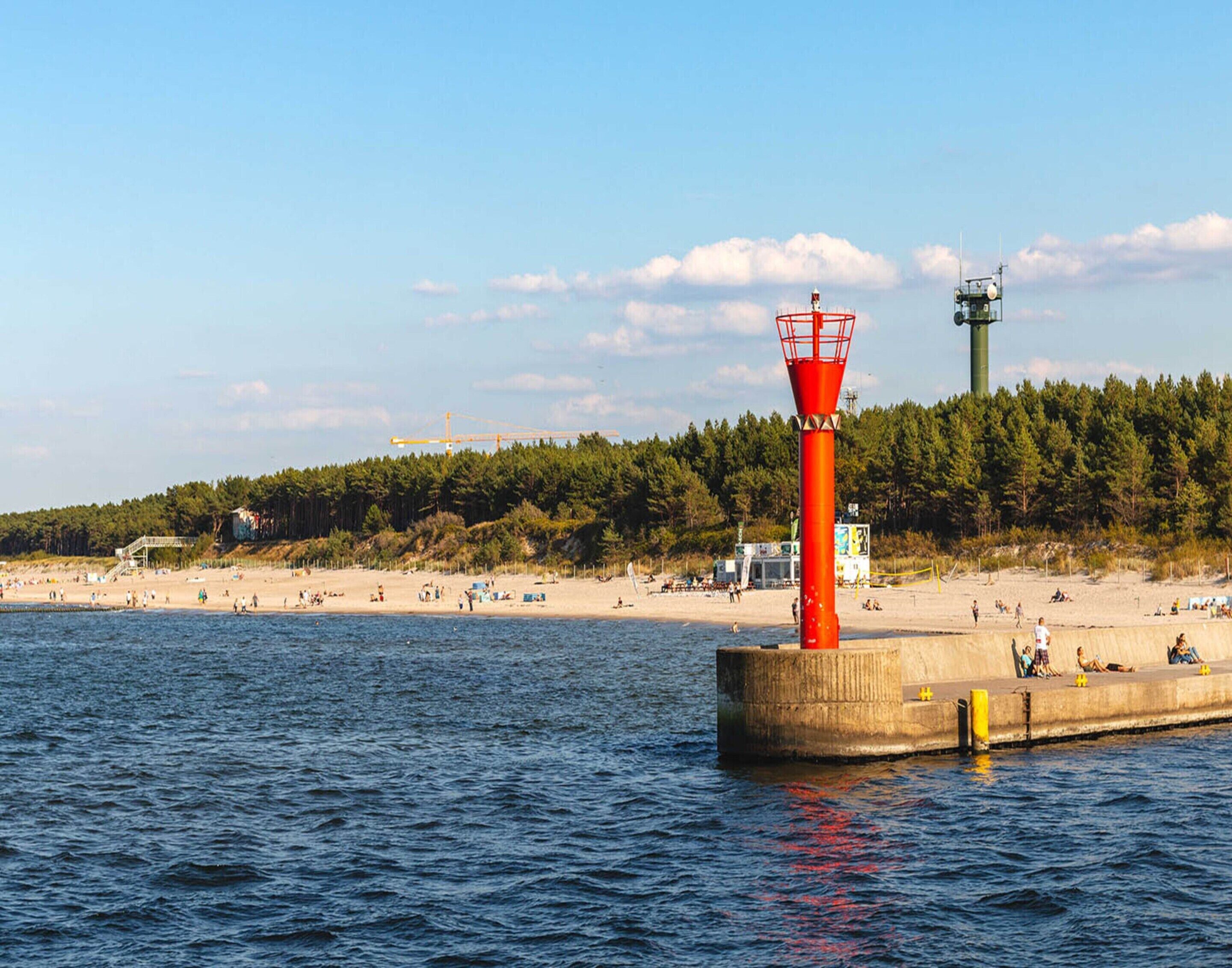 A lighthouse on a pier with a beach and forest in the background.