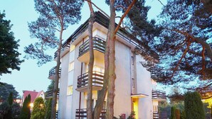 A multi-story residential building with balconies, surrounded by trees and a garden with orange flowers. - Mobile Home in Rogowo Near Baltic Beach (Trzebiatow)