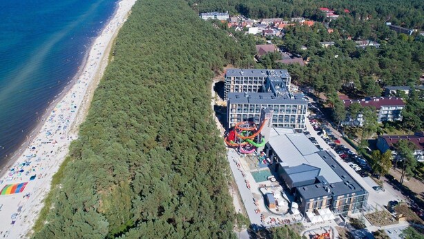 An aerial view of a coastal area with a beach, dense forest, and a modern building with a swimming pool and water slides. - Mobile Home in Rogowo Near Baltic Beach (Trzebiatow)