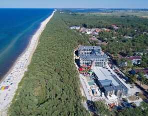 An aerial view of a coastal area with a beach, dense forest, and a modern building with a swimming pool and water slides. - Mobile Home in Rogowo Near Baltic Beach (Trzebiatow)