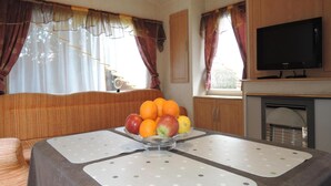A compact living space with a dining table set with fruit, a television, and a fireplace. - Mobile Home in Rogowo Near Baltic Beach (Trzebiatow)