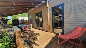 A wooden deck with a table and chairs, a sliding glass door, and a red lounge chair. - Mobile Home in Serignan With air Conditioning (Sérignan)