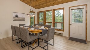 A dining area with a wooden table, grey upholstered chairs, and a hanging light fixture.