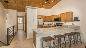 A modern kitchen with wooden cabinets, a stainless steel refrigerator, a built-in oven, and a large island with bar stools.